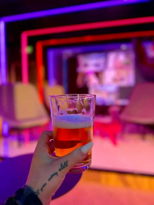 A glass of beer raised in the neon-lit Adway lounge