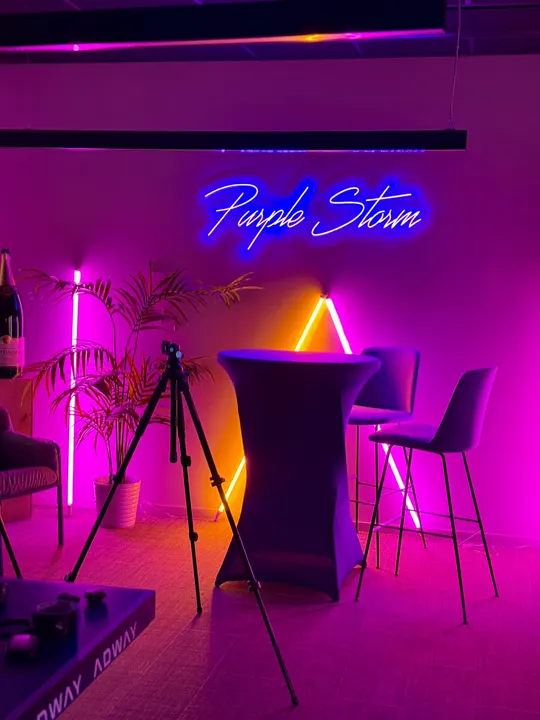 A neon sign reading Purple Storm above a high table and bar stools